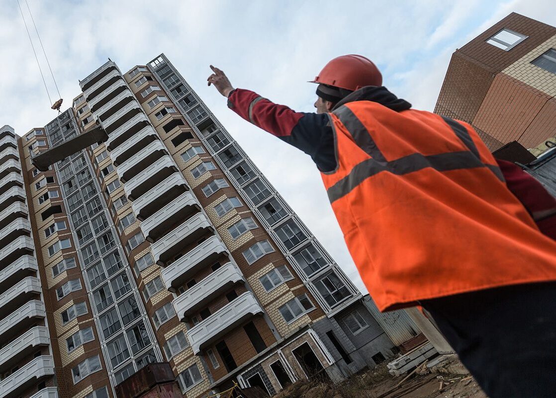 Новостройки и строитель в жилете и каске